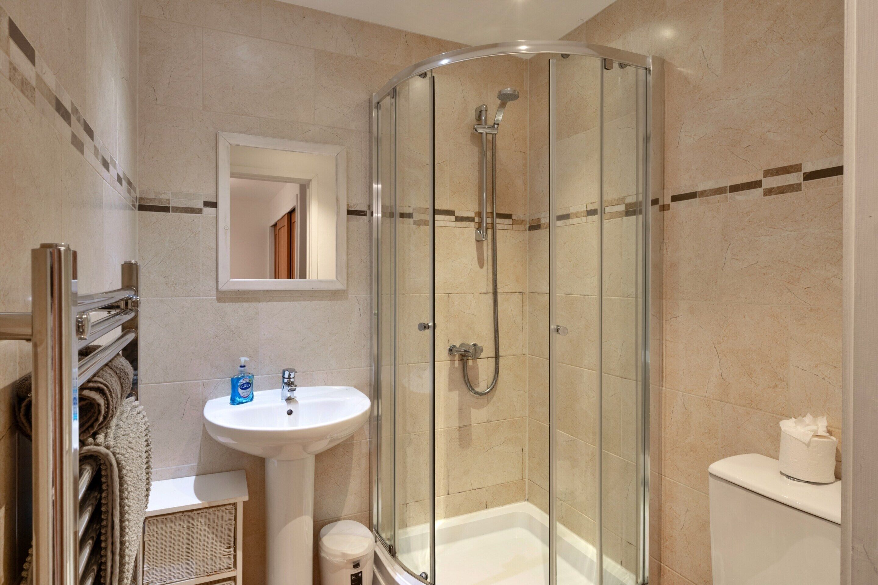 A modern bathroom with a glass-enclosed shower, a white sink, and a toilet.