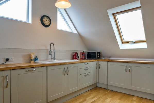 A kitchen with a skylight, a clock, and a microwave on the counter. - Stunning Broad Haven Beach House (Newquay)