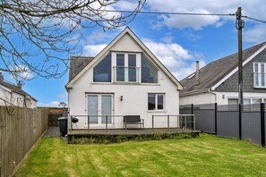 Ein zweistöckiges Haus mit geneigtem Dach, einem umzäunten Garten und blauem Himmel.