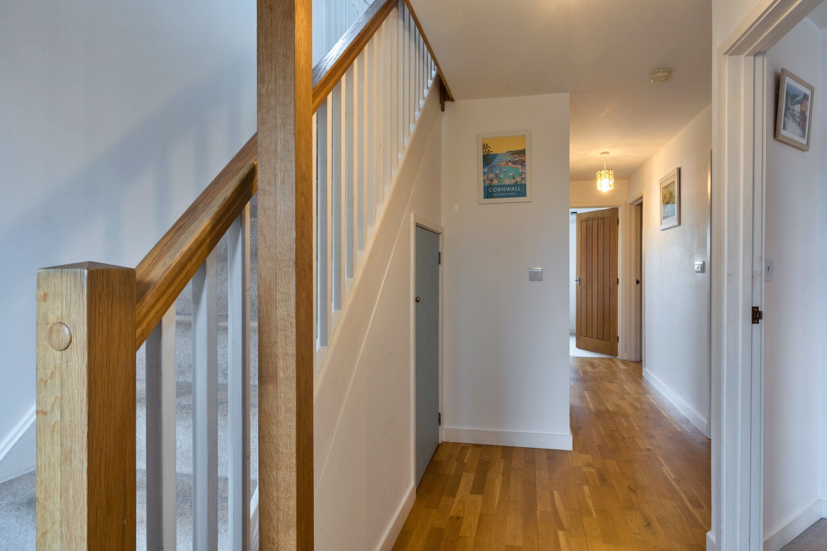 A hallway with a wooden staircase, white walls, and a wooden door at the end.