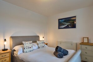 A neatly made bed with pillows, a bedside lamp, a radiator, and a framed picture on the wall. - Stunning Broad Haven Beach House (Newquay)