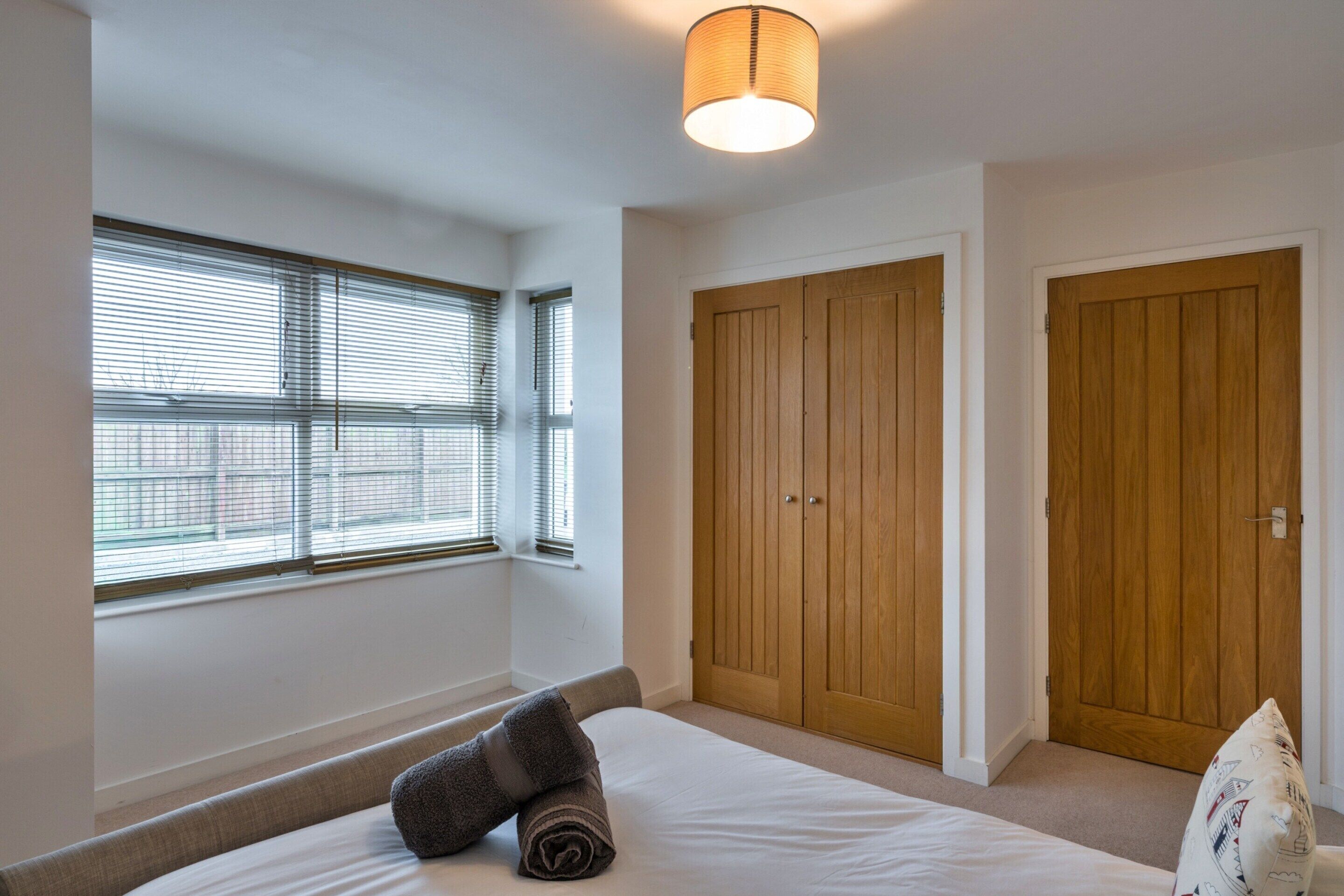 A bedroom with a bed, a window with blinds, a wooden wardrobe, and a door.