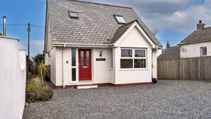 A single-story house with a red front door, a small porch, and a gravel driveway. - Stunning Broad Haven Beach House (Newquay)