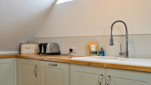 A kitchen with a wooden countertop, a toaster, a bread box, a bag of starter packs, a bottle of hand soap, and a faucet. - Stunning Broad Haven Beach House (Newquay)