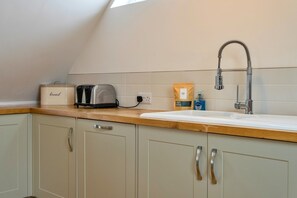 Eine Küche mit Holztischplatte, einem Toaster, einer Brotdose, einer Tüte Startersets, einer Handseifenflasche und einem Wasserhahn.