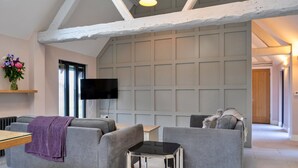 A modern living room with grey sofas, a small table, a flat-screen TV, and a decorative vase of flowers. - Charming Cottage for 4 in Dorset (Wimborne)