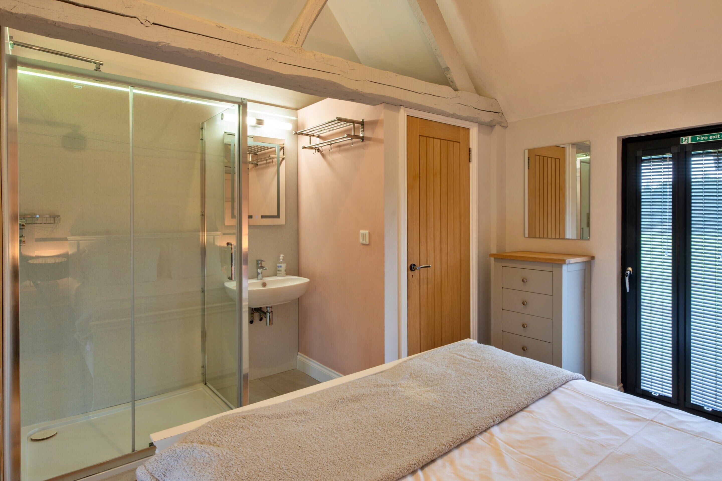 A bedroom with a bed, a glass shower enclosure, a wooden door, and a dresser.