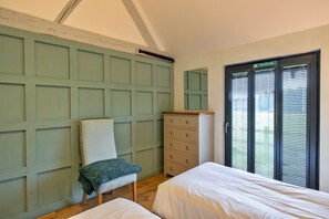 A bedroom with a bed, a chair, a dresser, and a door with a fire exit sign. - Charming Cottage for 4 in Dorset (Wimborne)