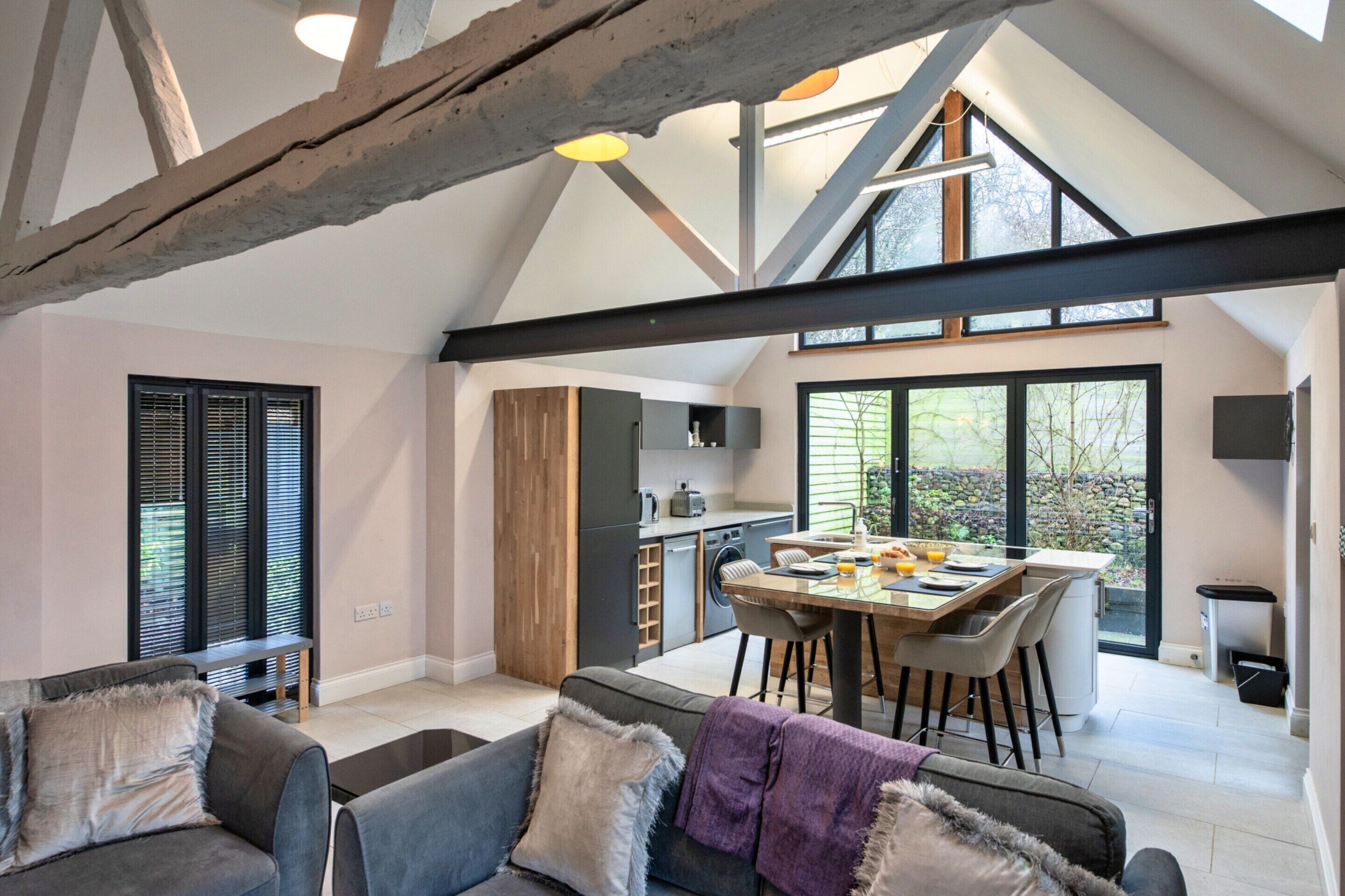 Un'ampia zona giorno con soffitto alto, un tavolo da pranzo con sedie, un divano e una cucina sullo sfondo.