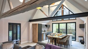 A spacious living area with a high ceiling, a dining table with chairs, a sofa, and a kitchen in the background. - Charming Cottage for 4 in Dorset (Wimborne)