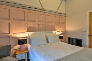 A bedroom with a bed, bedside lamps, a nightstand, a radiator, and a wooden door. - Charming Cottage for 4 in Dorset (Wimborne)