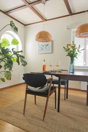 Un espace repas comprenant une table, des chaises, un luminaire suspendu, une fenêtre donnant sur un paysage et une plante.