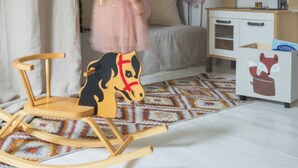 A child's room with a rocking horse, a bed, a dresser, and a fan.