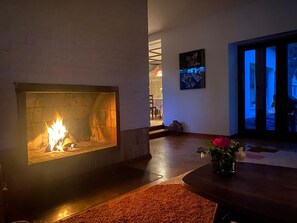 Ein Kamin mit Feuer, ein Essbereich mit Tisch und Stühlen sowie ein Gang zu einer Tür.