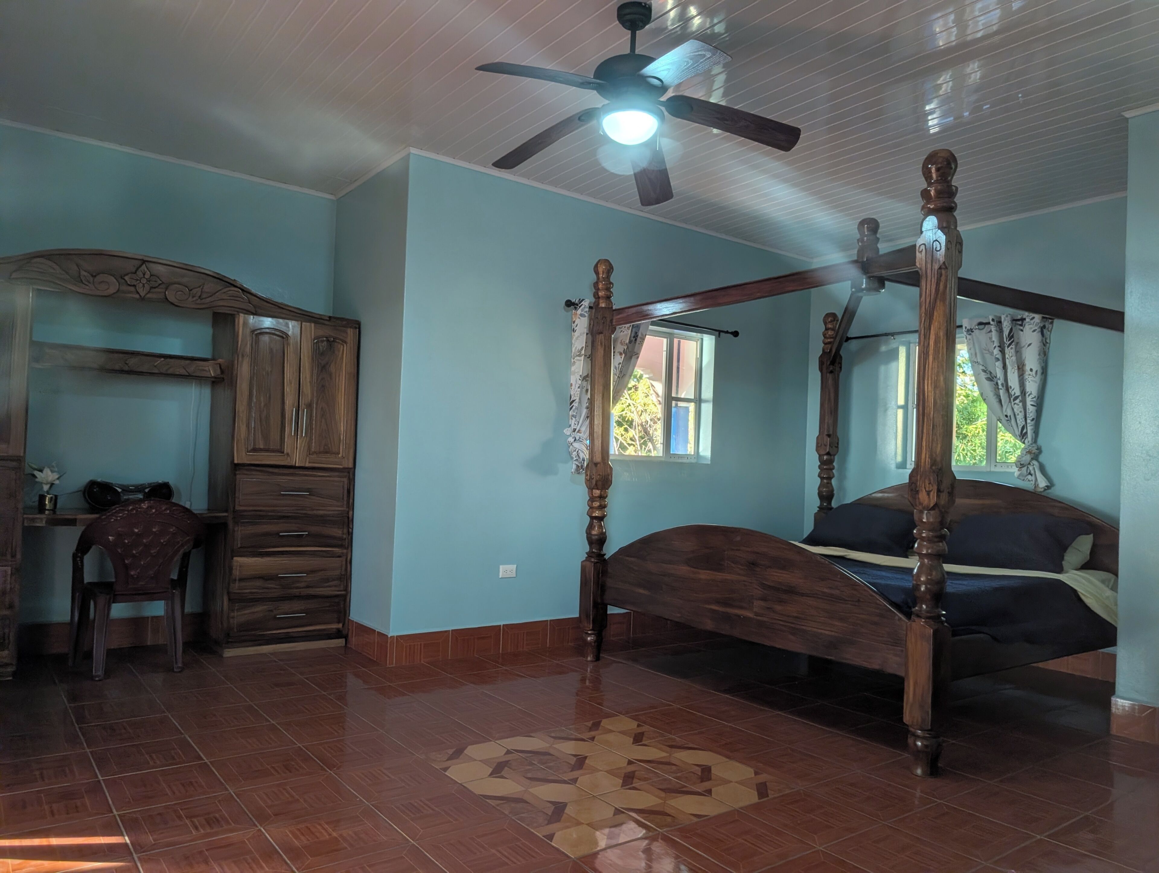 A bedroom with a four-poster bed, a ceiling fan, and a window with curtains.