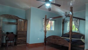 A bedroom with a four-poster bed, a ceiling fan, and a window with curtains.