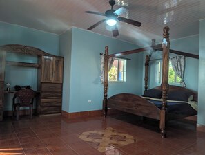 A bedroom with a four-poster bed, a ceiling fan, and a window with curtains.