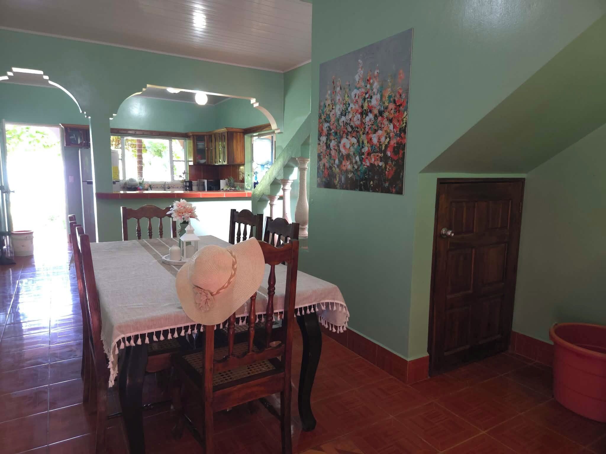 A dining area with a table set for two, a staircase, and a kitchen in the background.