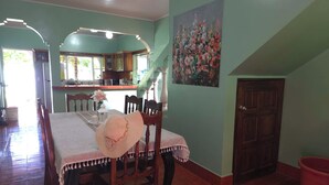 A dining area with a table set for two, a staircase, and a kitchen in the background.