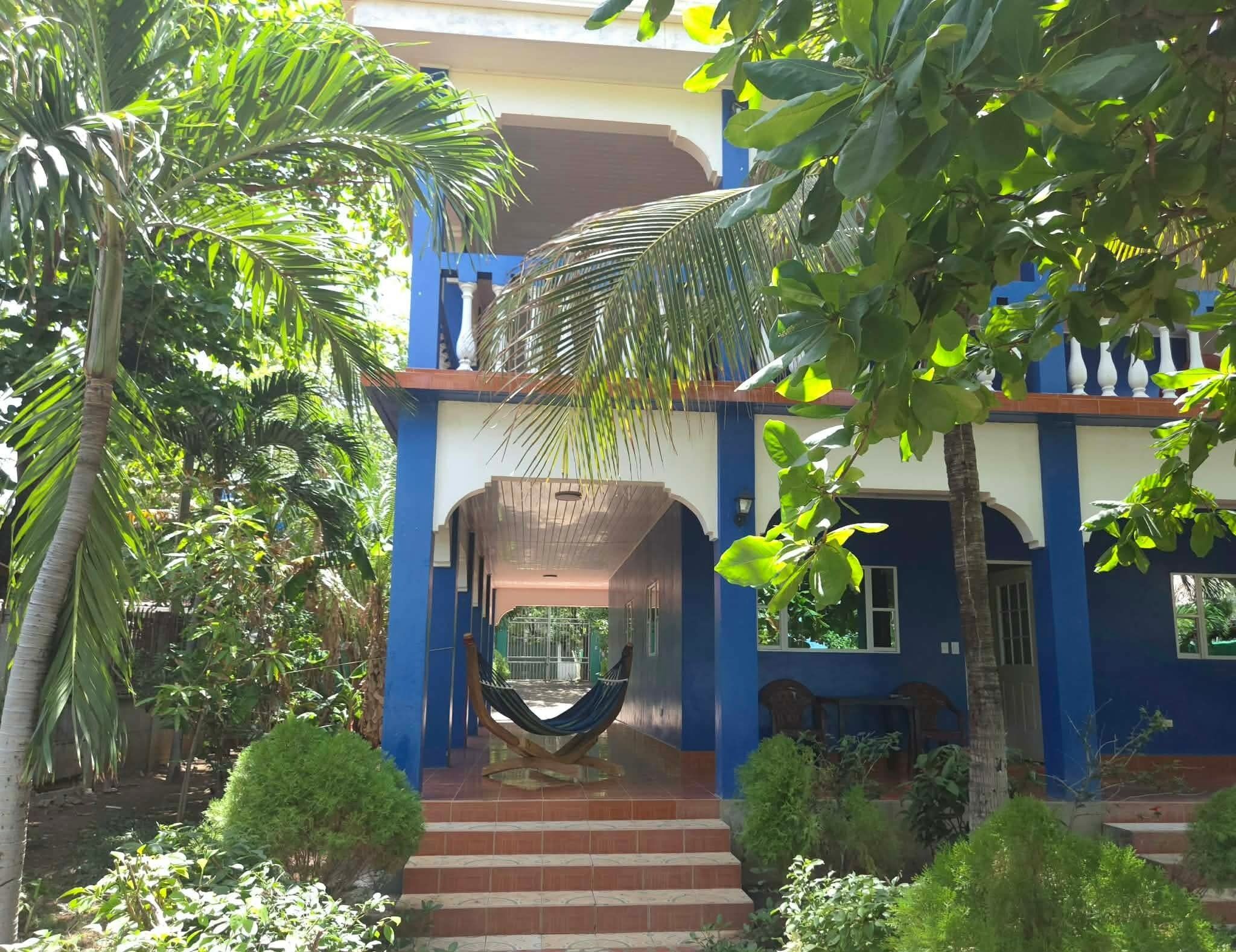 A two-story building with a blue exterior, a hammock on the porch, and a staircase leading to the entrance.
