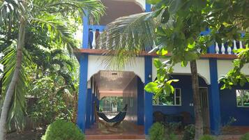 A two-story building with a blue exterior, a hammock on the porch, and a staircase leading to the entrance.