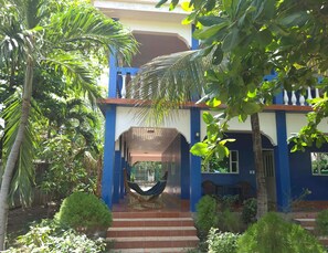 A two-story building with a blue exterior, a hammock on the porch, and a staircase leading to the entrance.