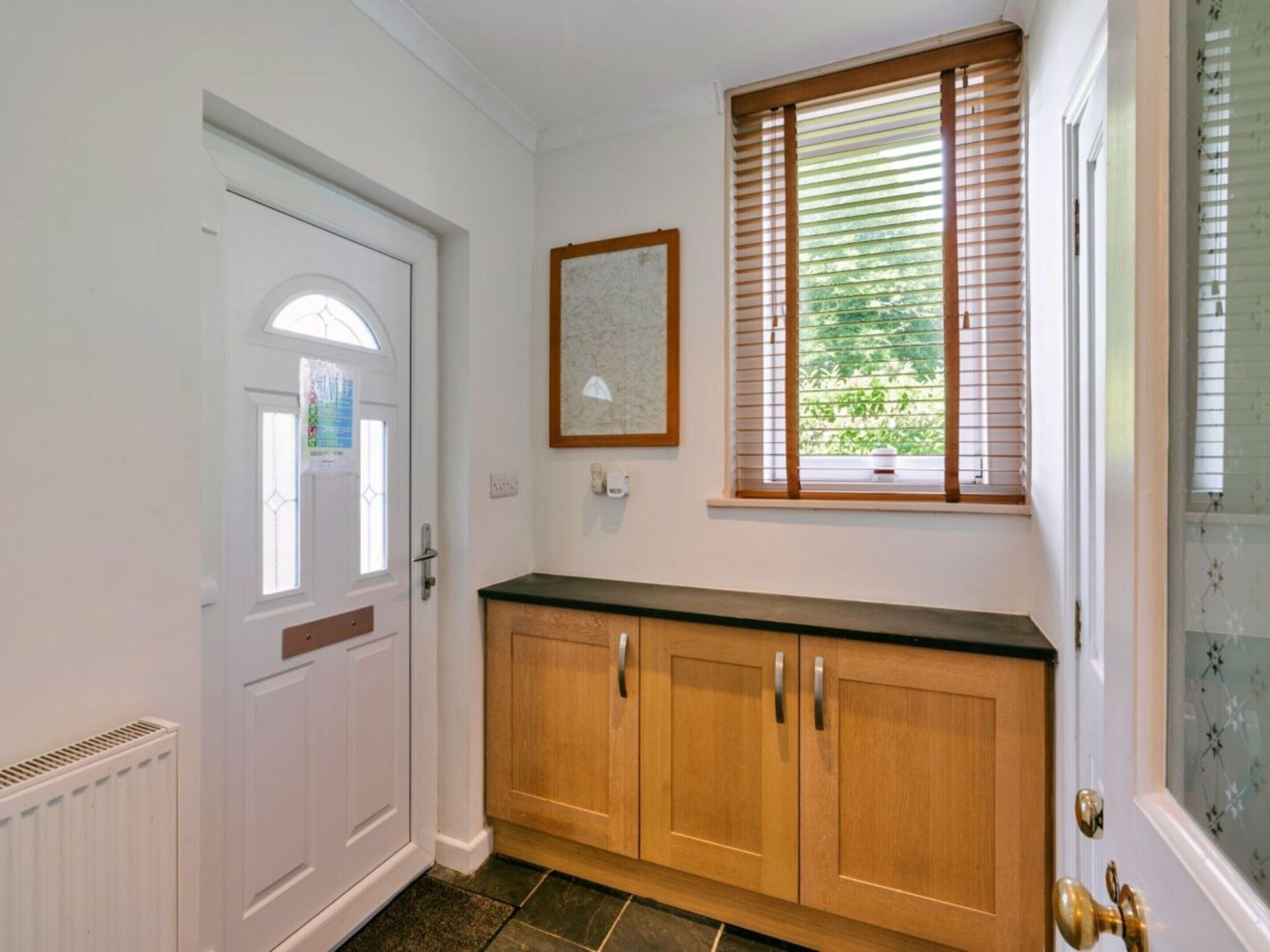 A hallway with a white door, a framed picture on the wall, and a window with blinds.
