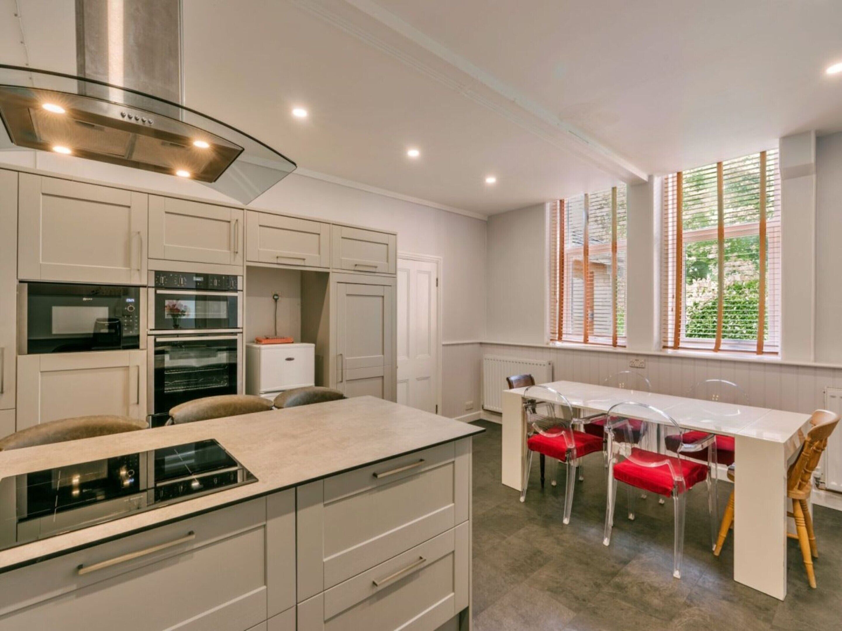 A modern kitchen with built-in appliances, a dining area with a table and chairs, and a window with blinds.