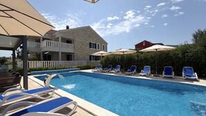 A swimming pool with lounge chairs and umbrellas, a stone building with a balcony, and a hedge in the background. - Two Bedroom Sea View Apartment Marisol (Mrljane)