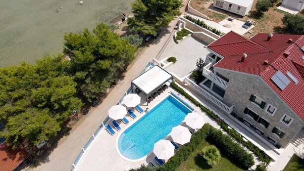 An aerial view of a coastal property with a swimming pool, lounge chairs, and a red-roofed building. - Two Bedroom Sea View Apartment Marisol (Mrljane)
