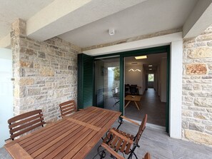 A wooden table and chairs in a room with stone walls and a sliding glass door leading to another space. - Two Bedroom Sea View Apartment Marisol (Mrljane)