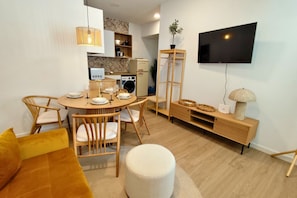 Ein modernes Wohnzimmer mit einem runden Esstisch, Holzstühlen, einer Couch, einem an der Wand montierten Fernseher und einer eingebauten Waschmaschine.