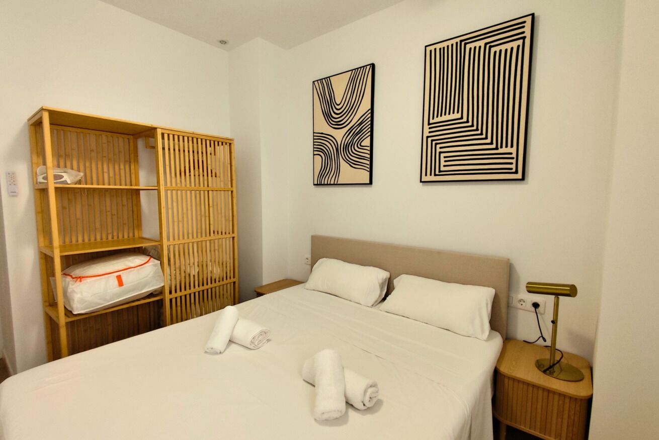 A hotel room with a bed, a wooden wardrobe, and two abstract paintings on the wall.