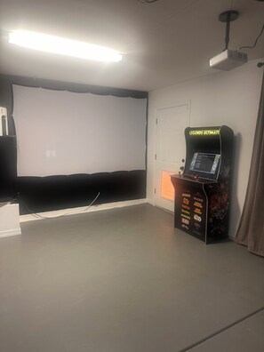 A room with a projector screen, a gaming console, and a door.