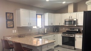 A modern kitchen with white cabinets, a stainless steel microwave, a black refrigerator, and a granite countertop. - Desert Oasis route 66 (Kingman)