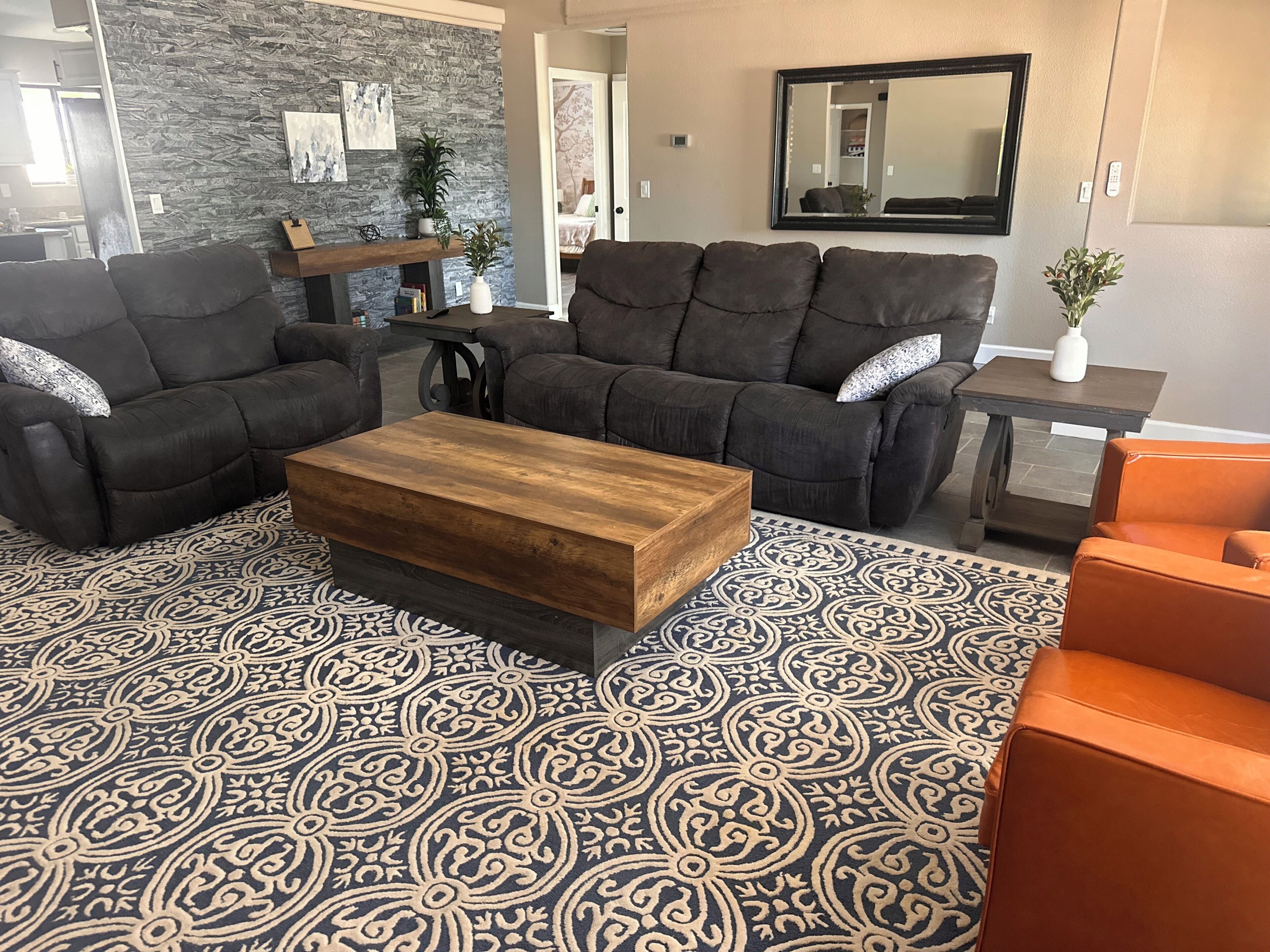 A living room with a dark brown sofa set, a wooden coffee table, patterned rug, and a small side table with a plant.