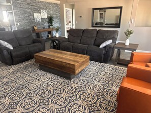 A living room with a dark brown sofa set, a wooden coffee table, patterned rug, and a small side table with a plant. - Desert Oasis route 66 (Kingman)