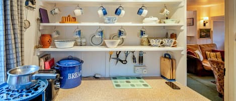 Une cuisine avec un plan de travail bleu, des ustensiles suspendus et divers accessoires de cuisine rangés sur des étagères.