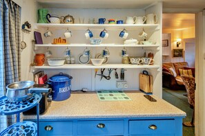A kitchen with a blue countertop, hanging utensils, and various kitchenware on shelves. - Historic Cornish Valley Cottage for 5 (Bude)