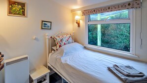 A bedroom with a bed, a window with a view of trees, a radiator, and a small stool. - Historic Cornish Valley Cottage for 5 (Bude)
