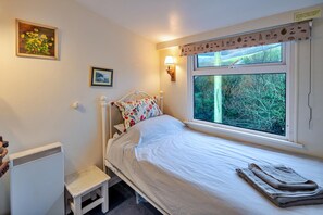 Ein Schlafzimmer mit Bett, einem Fenster mit Blick auf Bäume, einem Heizkörper und einem kleinen Hocker.