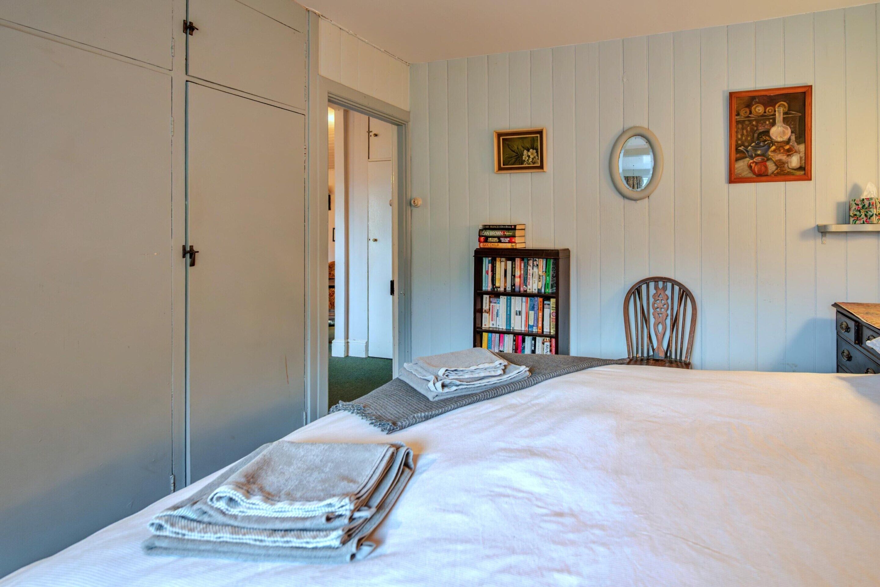 Ein Schlafzimmer mit Bett, Bücherregal, Stuhl, Schreibtisch und einer Tür.