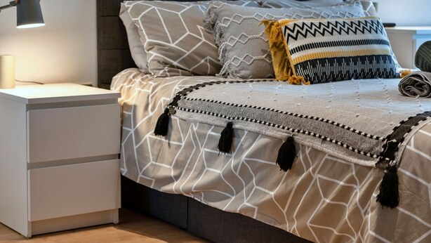A neatly made bed with a patterned bedspread, a decorative pillow, and a bedside lamp on a white nightstand. - Modern Plymouth Apartment Near The Hoe (Plymouth)
