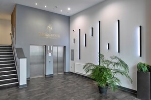 Ein modernes Interieur mit einer Treppe, Aufzügen und einer Rezeption mit dem Schild 'PEIRSON HOUSE APARTMENTS'.