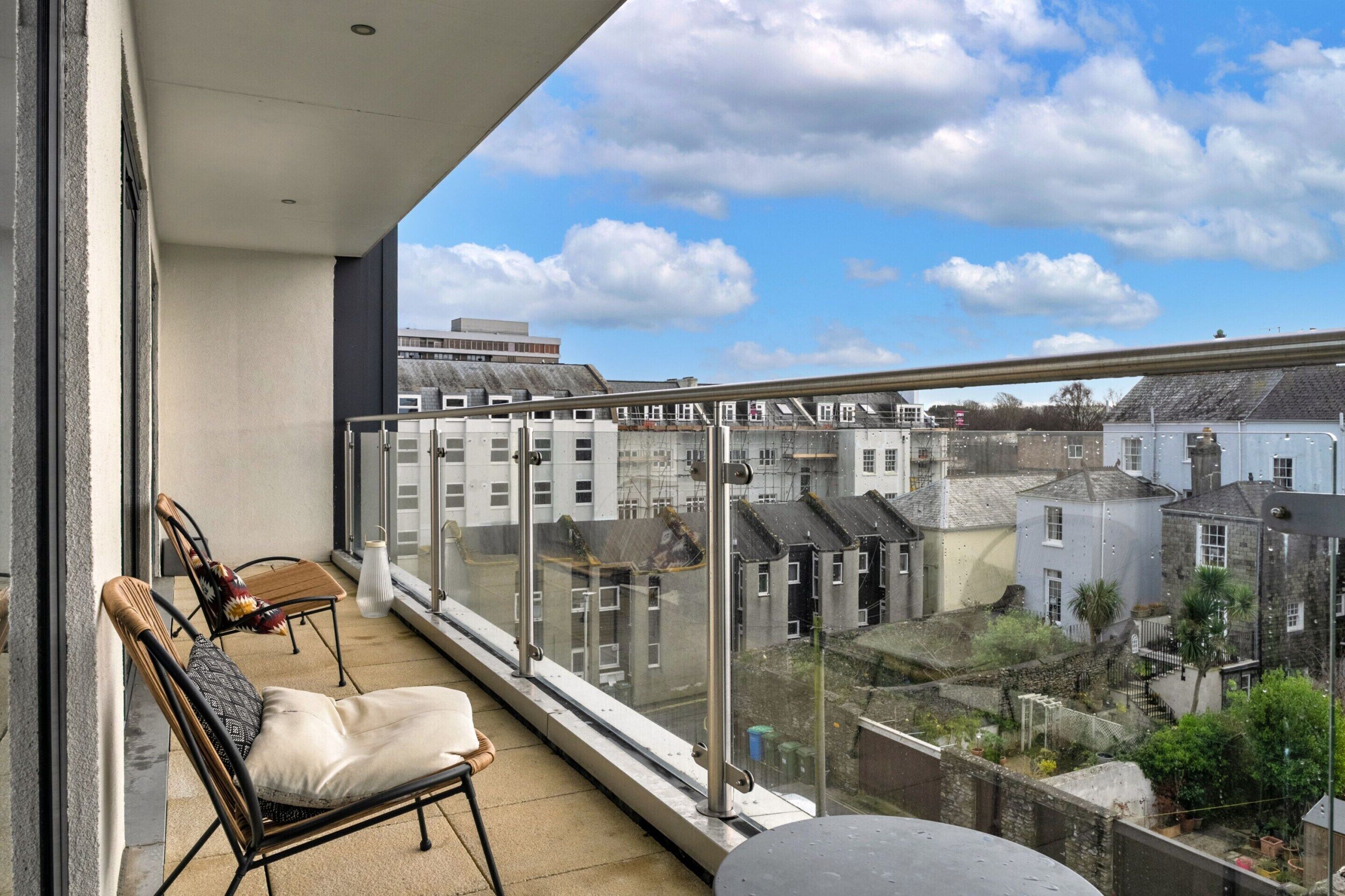 Ein Balkon mit Blick auf Wohnhäuser, ein Stuhl, ein Kissen und ein Glasgeländer.