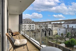 Ein Balkon mit Blick auf Wohnhäuser, ein Stuhl, ein Kissen und ein Glasgeländer.
