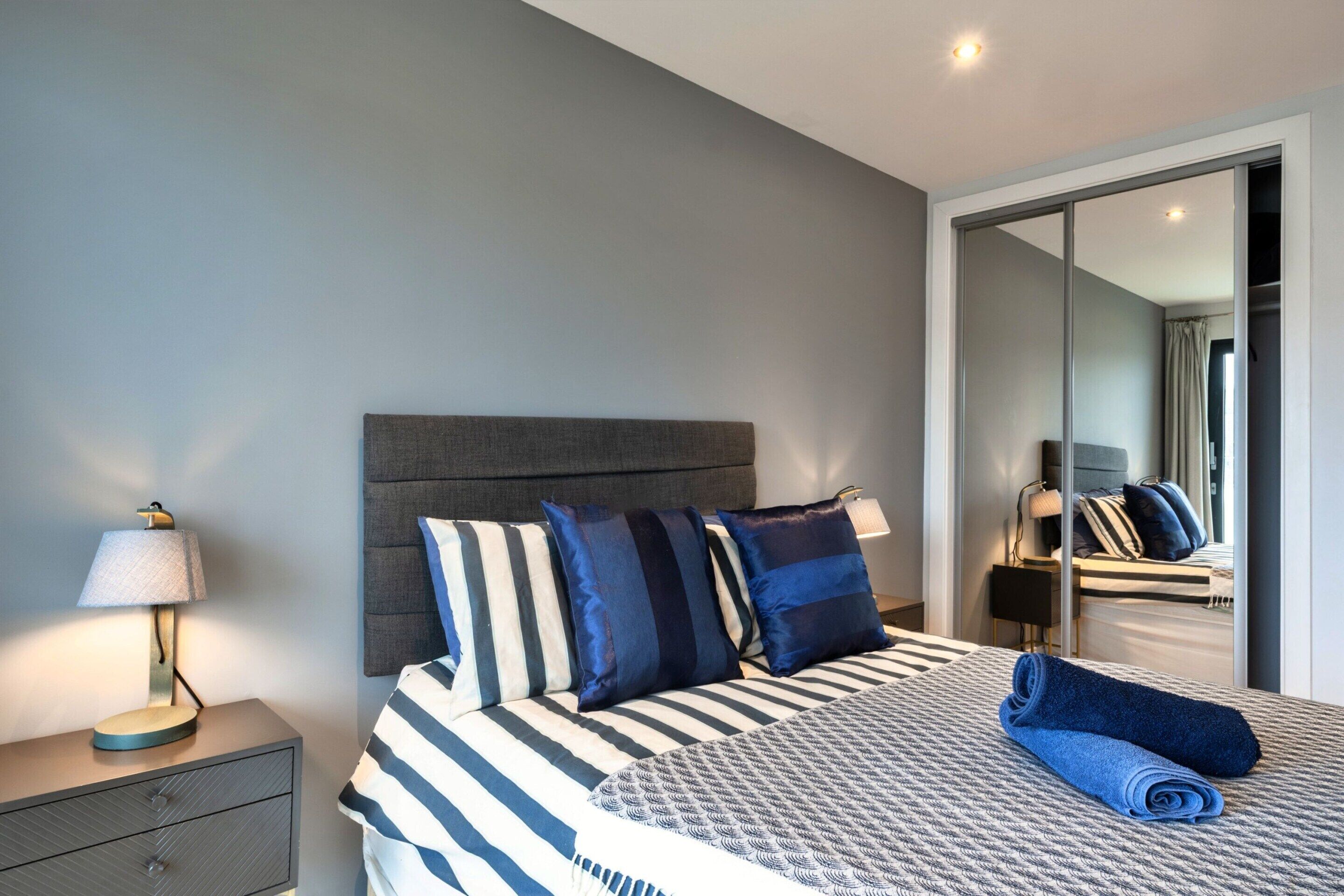 A neatly made bed with striped bedding and multiple pillows, a bedside lamp, and a folded towel on the bed.