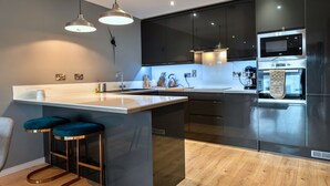 A modern kitchen with a central island, bar stools, stainless steel appliances, and pendant lighting. - Modern Plymouth Apartment Near The Hoe (Plymouth)