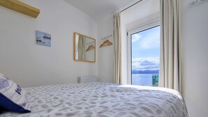 Un dormitorio con cama, espejo, radiador y vista al mar.