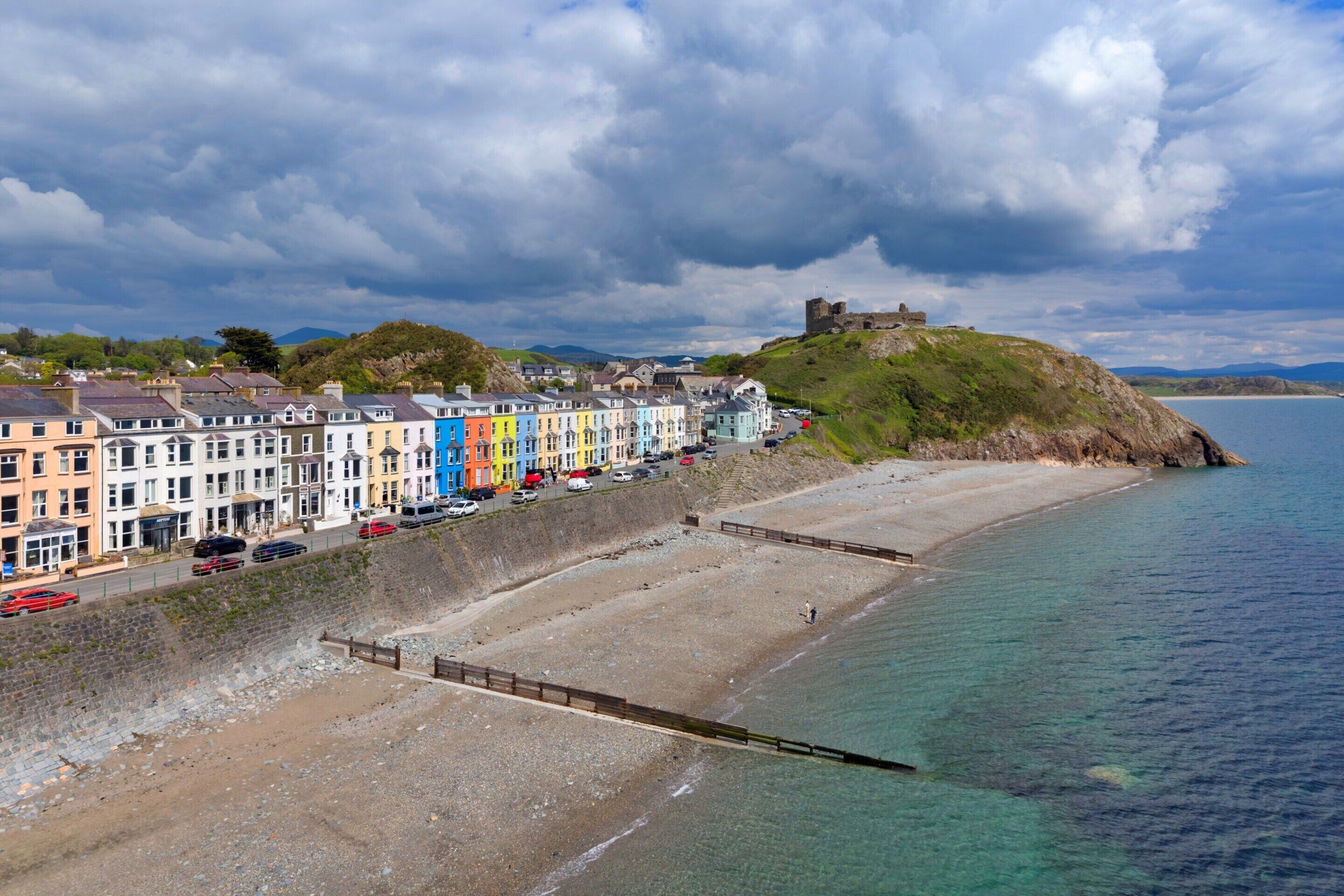 Uma cidade costeira com edifícios coloridos, uma praia e um castelo histórico numa colina.